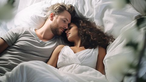 A close up of a couple lying in bed, surrounded by crisp, white bed linens.