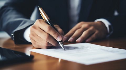 A close up of a man signing off on a loan document, showing the company's commitment to providing financial services.