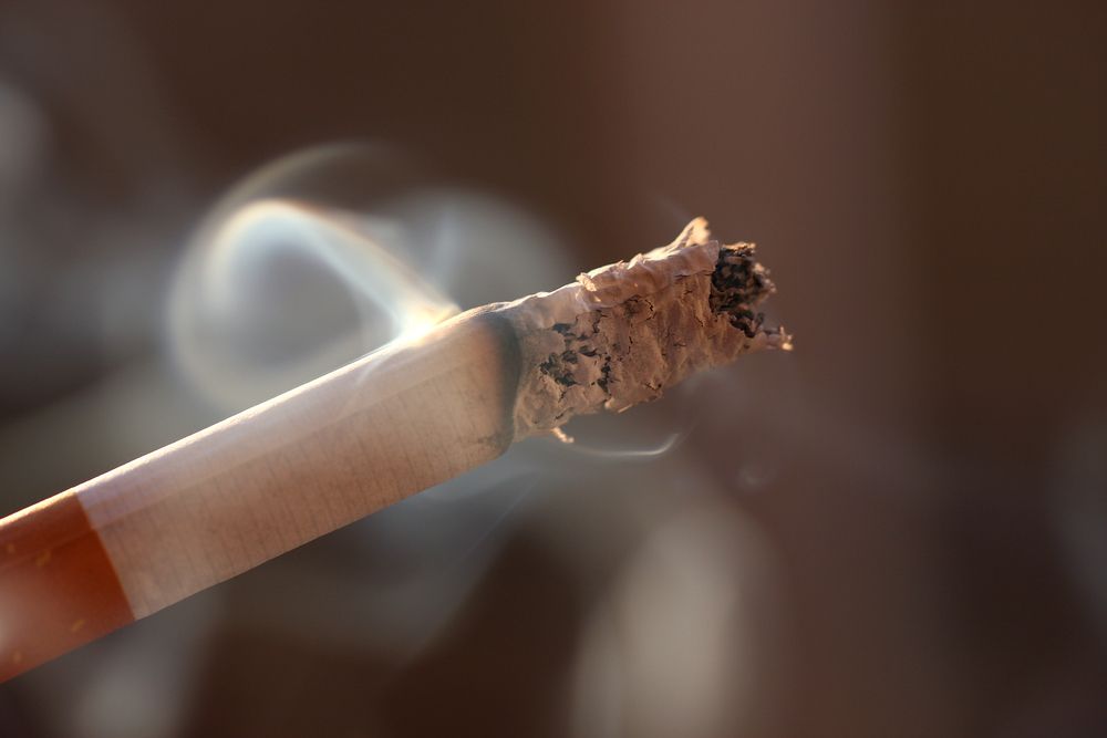 cigarette dark A smoking cigarette over a dark background, low key light Stock Photo