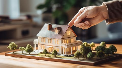 A real estate broker pointing to a house model, with the caption 'Real Estate-backed Loans Available.'.